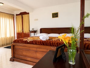 A hotel room with a wooden bed, a bedside table with a vase of flowers, and a mirror. - Channa Hotel and Rest Labookellie (Nuwara Eliya)