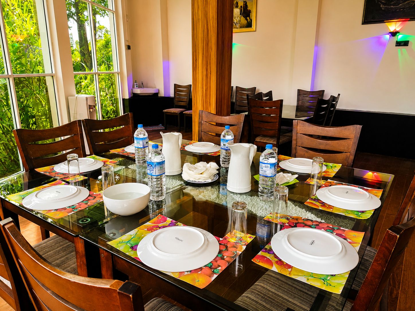 Uma sala de jantar com mesa de vidro, cadeiras de madeira e vista para o verde através de grandes janelas.