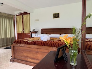 A hotel room with a wooden bed, a bedside table with a vase of flowers, a mirror, and a window with curtains. - Channa Hotel and Rest Labookellie (Nuwara Eliya)