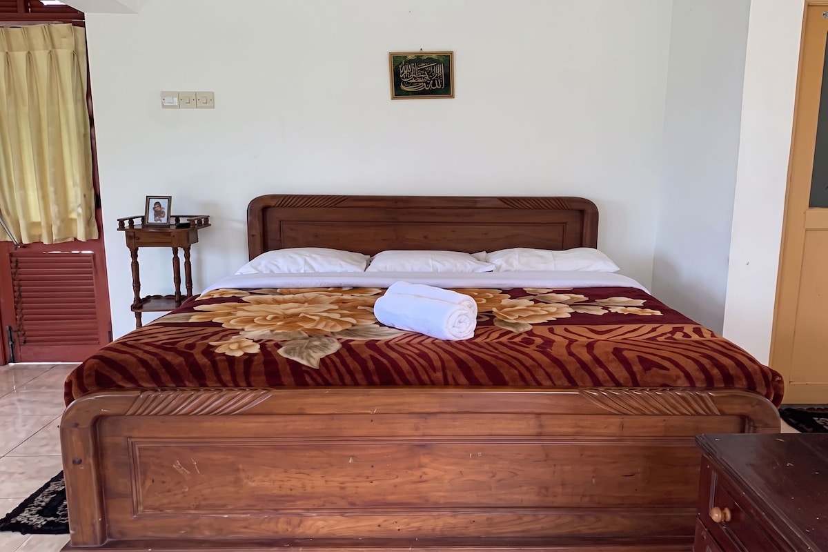 A neatly made bed with a floral bedspread, a wooden headboard, and a small bedside table with a framed photo.