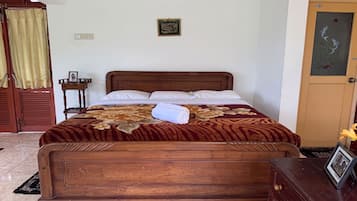 Cama bem arrumada com colcha florida, cabeceira de madeira e uma mesinha de cabeceira com uma foto emoldurada.
