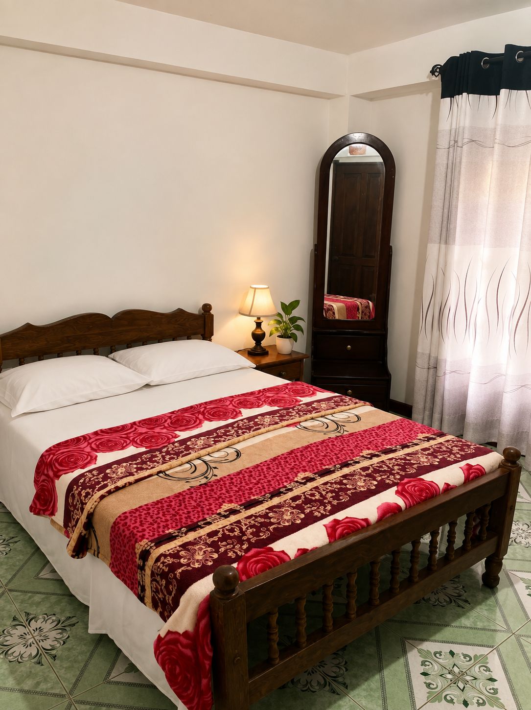 A bed with a wooden headboard, a bedside table with a lamp, a mirror, and a patterned bedspread.