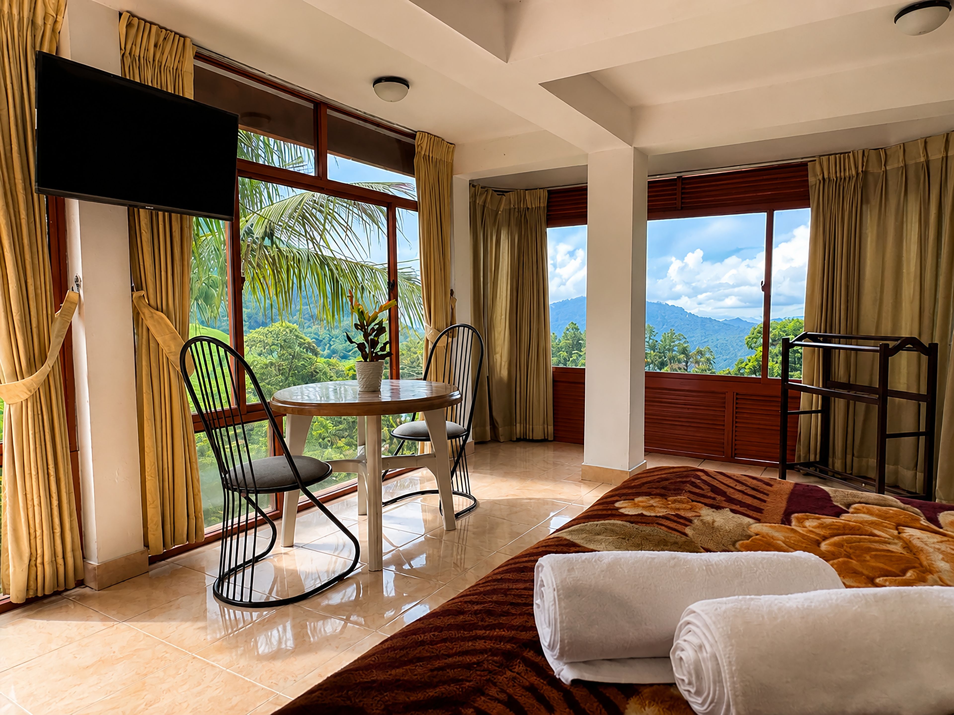Habitación de hotel con una cama, una mesa con sillas, un televisor y vistas a las montañas.