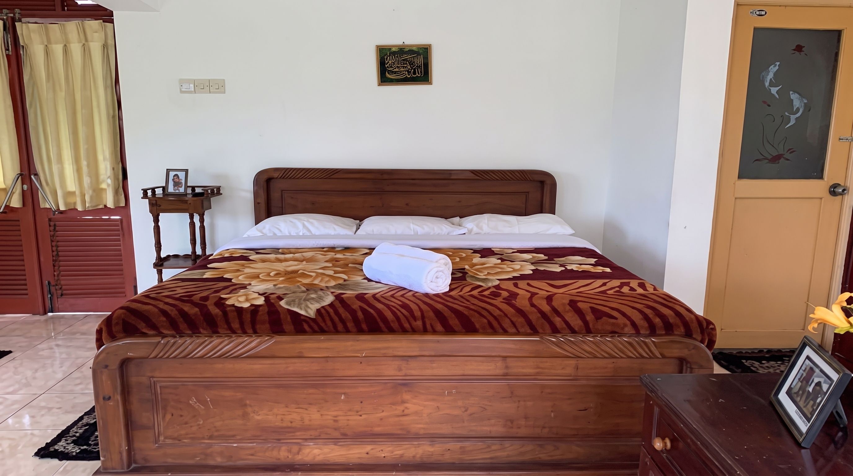 A neatly made bed with a floral bedspread, a wooden headboard, and a small bedside table with a framed photo.