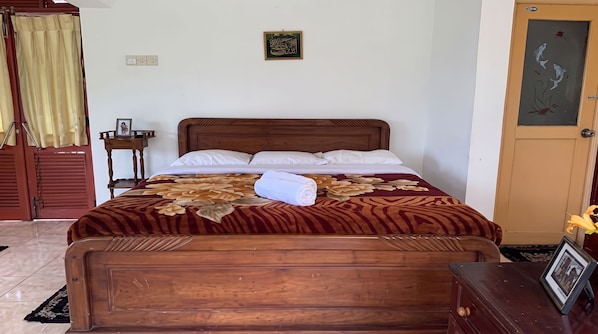 A neatly made bed with a floral bedspread, a wooden headboard, and a small bedside table with a framed photo. - Channa Hotel and Rest Labookellie (Nuwara Eliya)