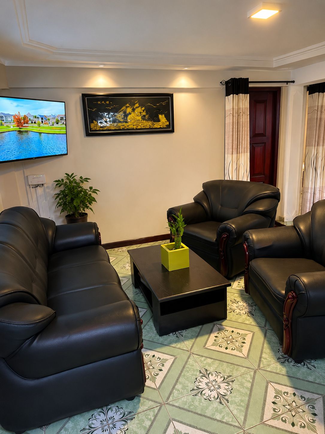 Uma sala de estar com um sofá de couro preto, uma mesa de centro com um vaso amarelo, uma televisão de tela plana e uma obra de arte emoldurada na parede.
