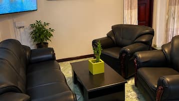 Uma sala de estar com um sofá de couro preto, uma mesa de centro com um vaso amarelo, uma televisão de tela plana e uma obra de arte emoldurada na parede.