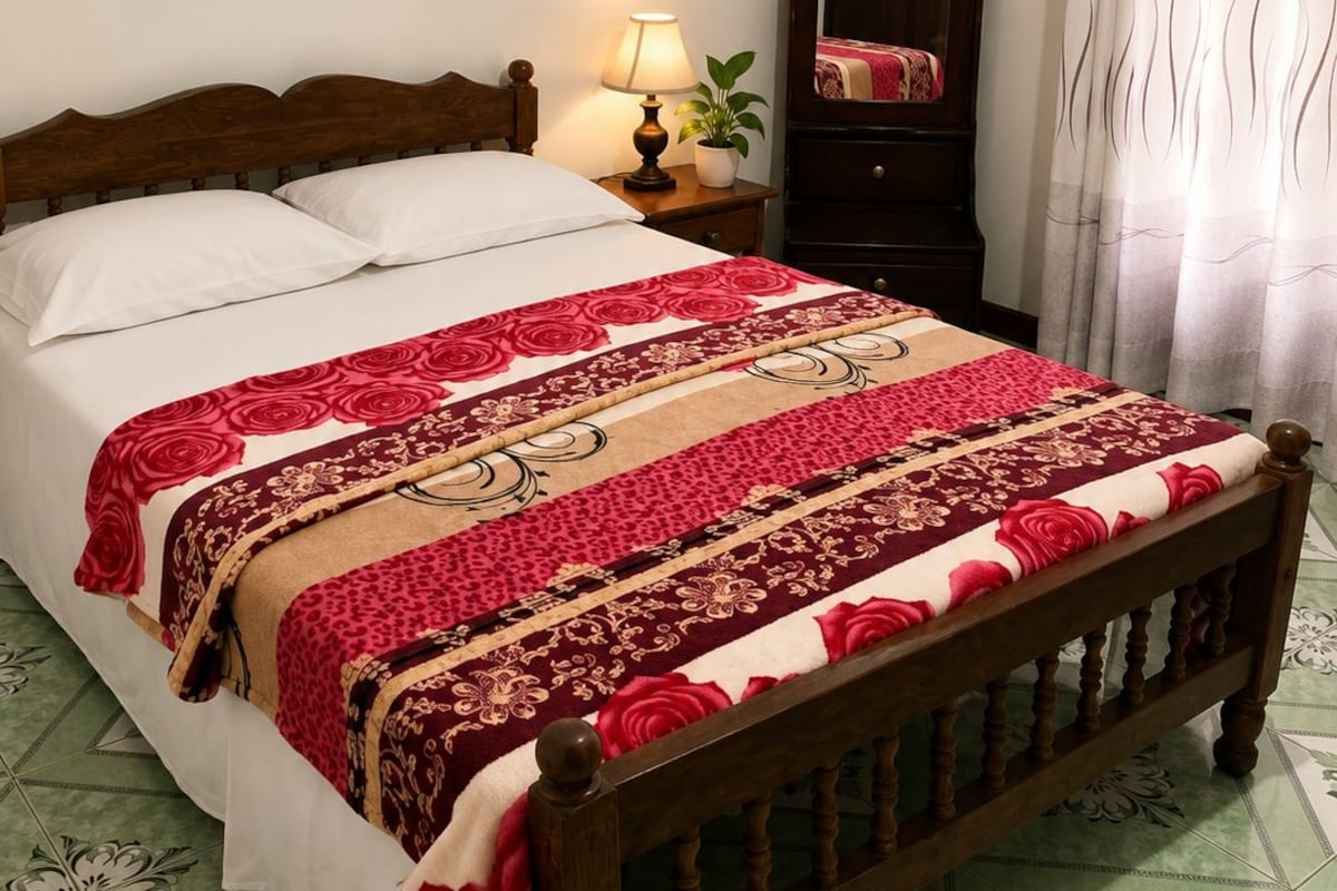 A bed with a wooden headboard, a bedside table with a lamp, a mirror, and a patterned bedspread.