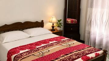 A bed with a wooden headboard, a bedside table with a lamp, a mirror, and a patterned bedspread.
