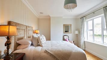 A bedroom with a large bed, bedside lamps, a mirror, and a view of the outdoors.