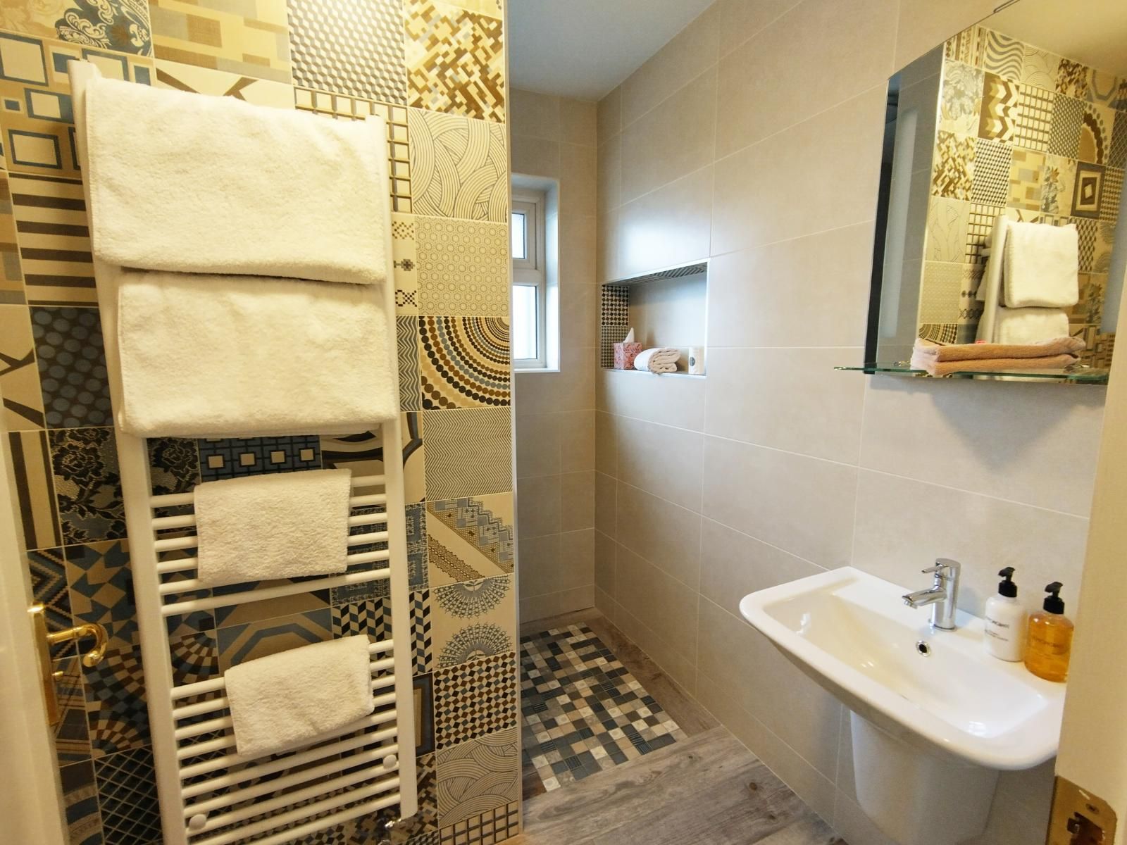 Une salle de bain avec un sol carrelé, un lavabo blanc, une étagère en verre avec des serviettes et un porte-serviettes avec plusieurs serviettes.