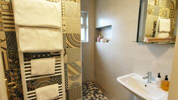 Une salle de bain avec un sol carrelé, un lavabo blanc, une étagère en verre avec des serviettes et un porte-serviettes avec plusieurs serviettes.