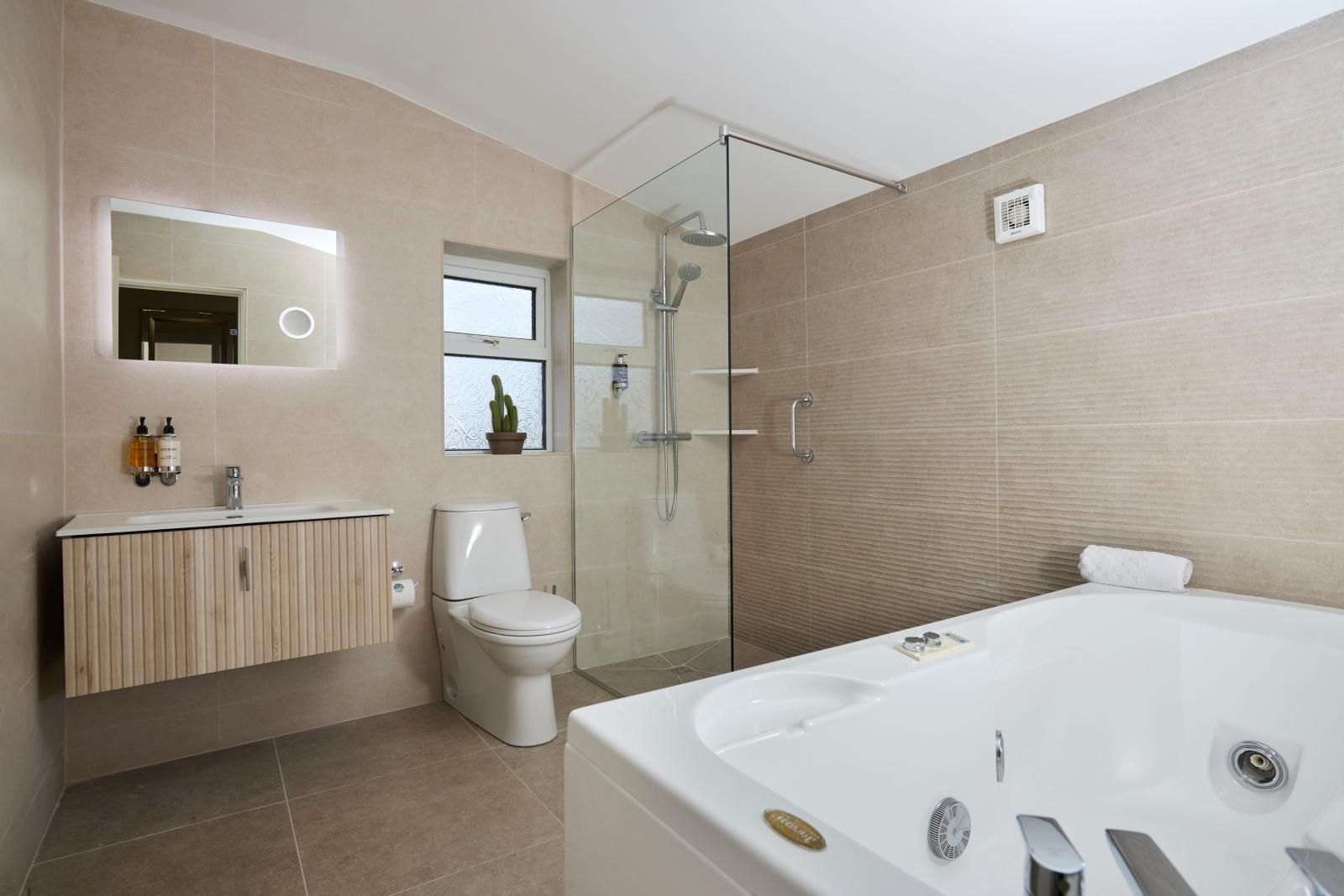 A modern bathroom with a glass-enclosed shower, a freestanding bathtub, and a vanity with a mirror and two bottles of soap.
