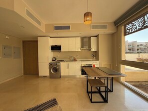A modern kitchen with built-in appliances, a dining area with a bench, and a large window offering a view of the outside. - Cozy 1BR GF Mangroovy Residence (Hurghada)