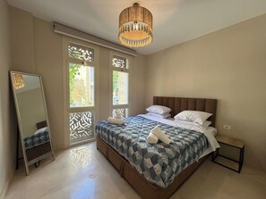 A bedroom with a bed, a bedside table, a mirror, and a hanging light fixture. - Cozy 1BR GF Mangroovy Residence (Hurghada)