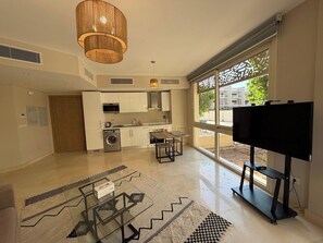 A modern kitchen with white cabinets, a washing machine, and a dining area with a glass table. - Cozy 1BR GF Mangroovy Residence (Hurghada)