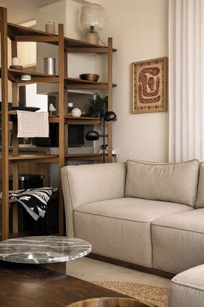 Een woonkamer met een beige bank, een houten boekenkast, een marmeren salontafel en een wandlamp.