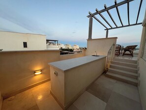 A rooftop terrace with a bar area, outdoor seating, and a staircase leading to an upper level.