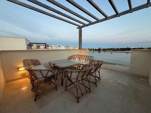 A terrace with wicker furniture and a table, overlooking a body of water and distant buildings. - Luxury 4BR Cyan Villa • Private Pool (Hurghada 2)