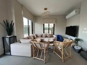 A modern living room with a sofa, two wicker chairs, a coffee table, a TV, and a large window.