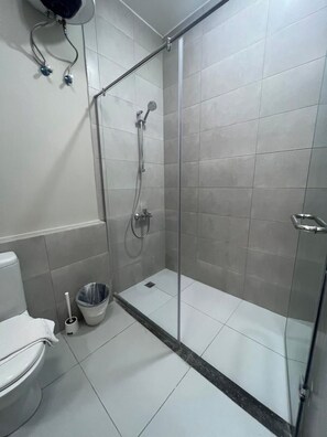 Un baño con ducha de vidrio, inodoro y un balde.