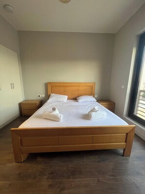 Ein großes Bett mit hölzernem Kopfteil und Fußteil, zwei Nachttische und ein Fenster mit Jalousien.