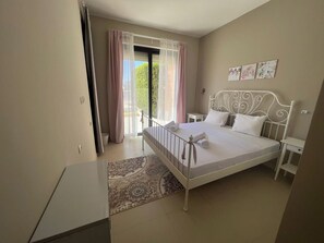 A bedroom with a bed, a bedside table, a nightstand, a window with curtains, and a door. - Tawila 3BR Family Townhouse • Lagoon Retreat Villa (Hurghada 2)