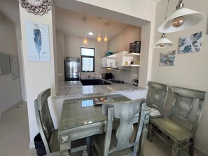 Una zona pranzo con tavolo e sedie, una cucina sullo sfondo e un orologio al muro.