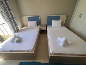 Camera d'albergo con due letti singoli, ognuno con testiera, comodino e asciugamano bianco arrotolato.
