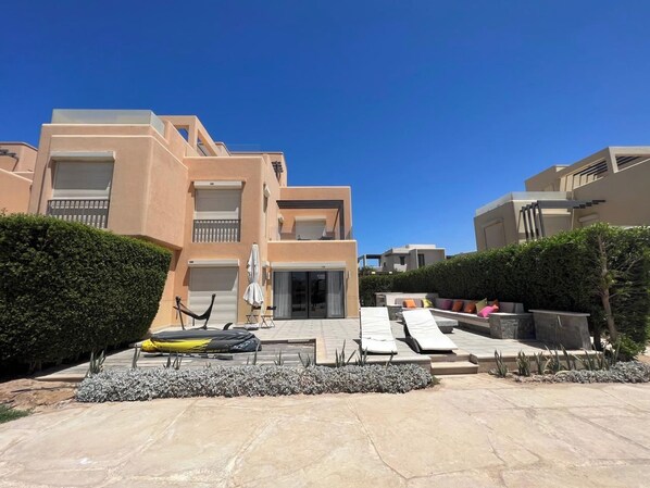 Un moderno edificio residenziale a più piani con una zona patio arredata con poltrone relax e un'amaca.