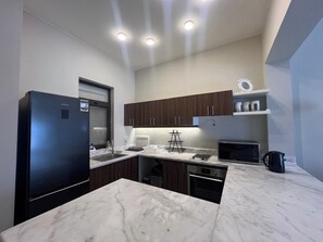 A modern kitchen with a refrigerator, microwave, kettle, and wooden cabinets.
