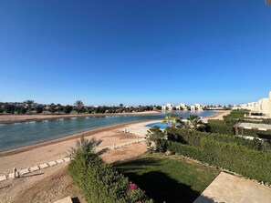 Vista a la orilla del río con piscina, zonas verdes y edificios al fondo.