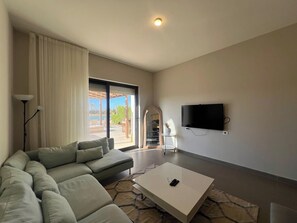 A modern living room with a sectional sofa, a coffee table, and a flat-screen TV mounted on the wall.