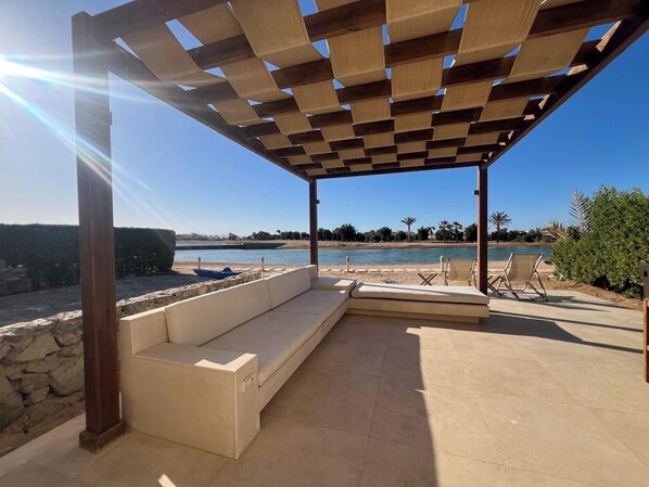 Un espacio de estar techado al aire libre con vista a un cuerpo de agua y una piscina.