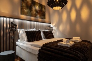 Ein modernes Hotelzimmer mit Bett, einem Kopfende mit vertikalen Linien, einem an der Wand befestigten Kunstwerk und einer außergewöhnlichen Pendelleuchte.