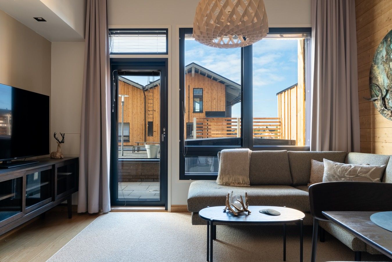 Una sala de estar moderna con televisor, sofá, mesa de centro y vista a un edificio de madera.