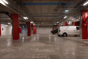 Eine mehrgeschossige Parkgarage mit roten Säulen, einem weißen Lieferwagen und einem beschädigten Fahrzeug.