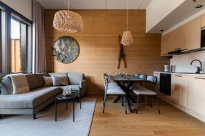 Uma sala de estar moderna com sofá, mesa de centro e área de jantar com cadeiras. Uma parede de madeira com um prato decorativo e duas luminárias pendentes.