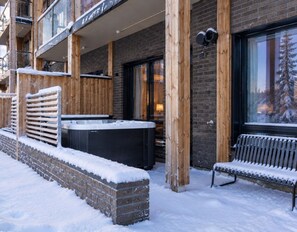 Ein Gebäude mit Ziegelverkleidung, Holzbalken, einem Whirlpool und einer mit Schnee bedeckten Bank.