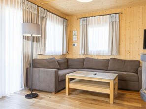 A cozy room with a sectional sofa, a small wooden coffee table, a floor lamp, and curtains on the windows. - One-bedroom Cabin (Sankt Georgen am Kreischberg)