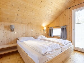 A wooden cabin bedroom with two beds, a window with curtains, and a wall-mounted light fixture. - One-bedroom Cabin (Sankt Georgen am Kreischberg)