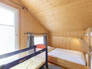 Eine Holzhütte mit Etagenbett, einem Vorhangfenster und einer Holzbalkendecke.