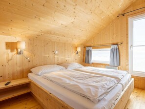 A wooden cabin room with a bed, two wall-mounted lamps, a window with curtains, and a shelf. - One-bedroom Cabin (Sankt Georgen am Kreischberg)