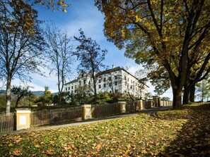 Ein großes Gebäude mit vielen Fenstern und einer symmetrischen Fassade, umgeben von Bäumen und einem Zaun.