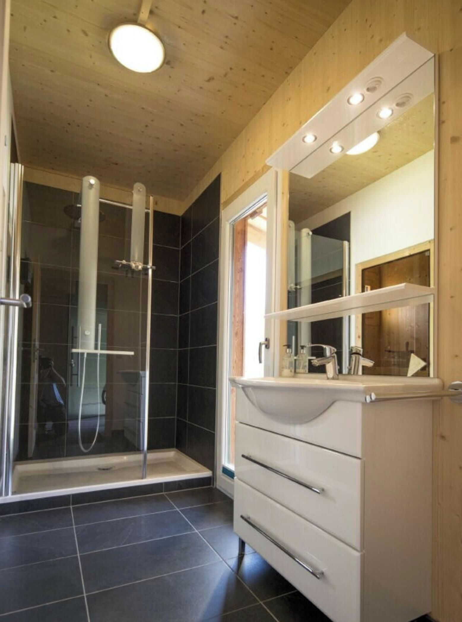 A modern bathroom with a glass shower enclosure, a vanity with a mirror, and a tiled floor.