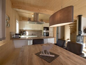 A modern kitchen with wooden cabinets, a central island, and a dining area with a wooden table and chairs. - Cabin With 1 Bedroom (Sankt Georgen am Kreischberg)