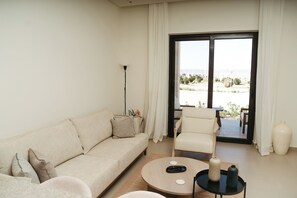 Un salón con sofá, sillón, mesa de centro y vistas al exterior a través de un ventanal corredero.