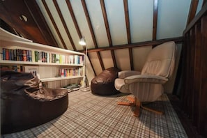 A cozy reading nook with a leather bean bag, a cushioned chair, and a bookshelf filled with books.