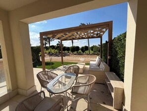 An outdoor patio with a pergola, seating area, and a view of a landscaped garden. - Cyan Elegant 3BR Golf View Escape (Hurghada)