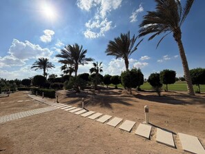 A pathway leading through a landscaped area with palm trees and trimmed bushes. - Cyan Elegant 3BR Golf View Escape (Hurghada)